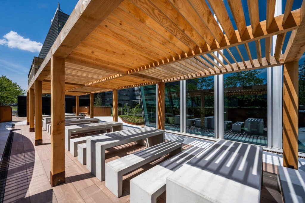 Overdekt terras met betonnen picknicktafels aan de David Ricardostraat, naast een modern kantoorgebouw.